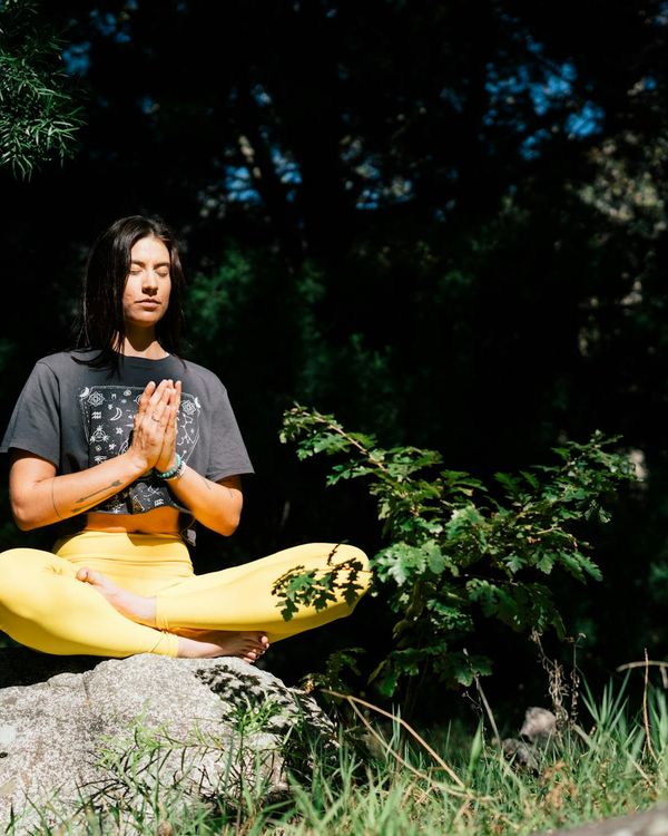 Woman sitting in a lotus pose and practicing breathing exercises outdoors.